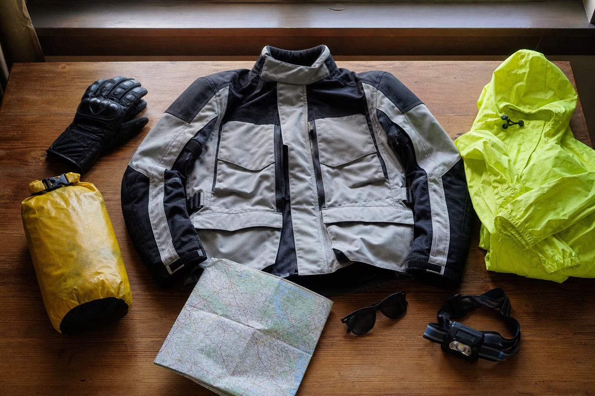 Flat-lay of riding gear and travel essentials packed for the Ha Giang Loop, including helmet, gloves, jacket and dry bag